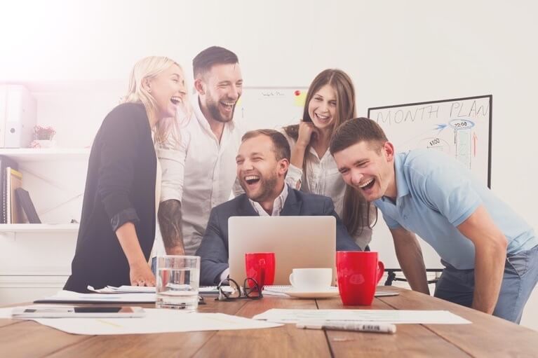 Eine Gruppe von fünf Personen steht lachend um einen Laptop