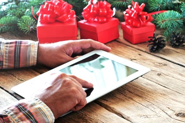 Männerhände mit einem Tablet vor Weihnachtsgeschenken